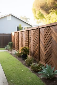 a wooden fence in front of a house with green grass and plants on the side