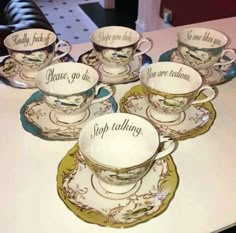 six tea cups and saucers with words on them sitting on a counter top next to each other