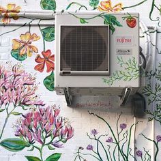 an air conditioner mounted to the side of a wall with flowers painted on it