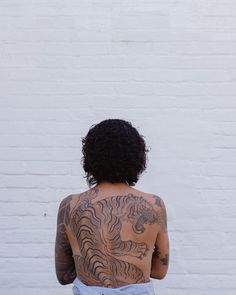 a woman with tattoos on her back standing in front of a white brick wall