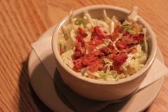 a white bowl filled with lettuce and bacon on top of a wooden table