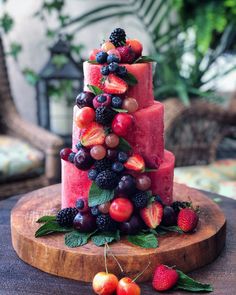 a watermelon cake with berries and cherries on the top is sitting on a wooden platter