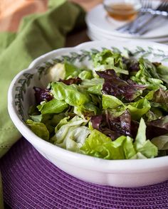 a white bowl filled with lettuce on top of a purple place mat