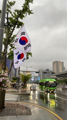 two flags hanging from a pole on the side of a road in front of a green bus