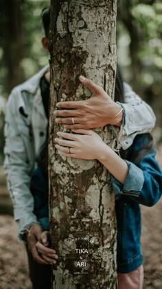 a man and woman hugging each other next to a tree in the middle of the woods