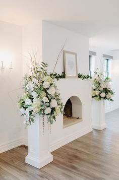 the fireplace is decorated with white flowers and greenery for an elegant touch to the room