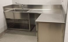 a stainless steel kitchen sink and counter in a room with white tiles on the walls