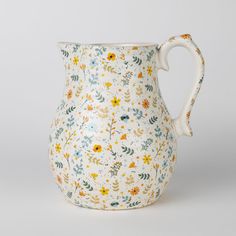 a white vase with yellow and blue flowers on the outside, sitting in front of a gray background