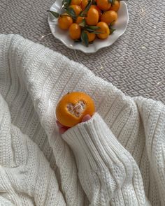 a person holding an orange in their hand next to a bowl of oranges on the floor