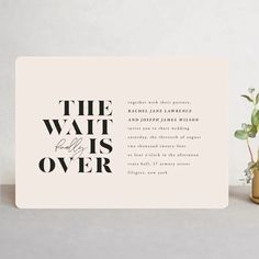 the wait is over wedding card in black and white on a table next to a potted plant