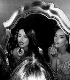 black and white photograph of two women brushing their teeth in front of a large mirror