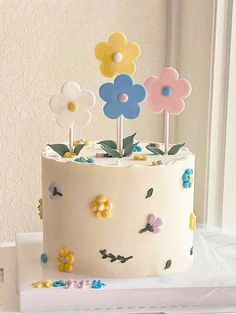 a white cake with flowers on it sitting on top of a table next to a window