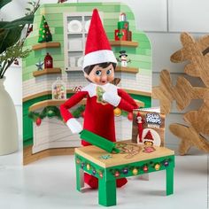 an elf is sitting in front of a table with christmas decorations on it and holding a candy bar