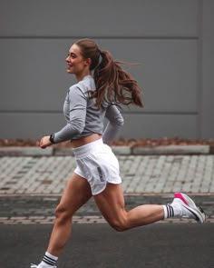 a woman is running on the street with her hair blowing in the wind and wearing white shorts