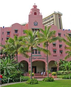 a pink building with palm trees in front of it and people walking around the yard