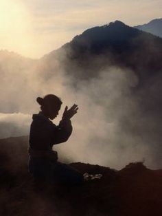 a person sitting on top of a mountain next to a fog filled valley with mountains in the background