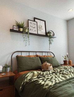 a bed with green comforter and pillows in a bedroom next to two plants on the wall