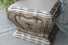 an ornately decorated silver chest on the sidewalk next to a planter and door