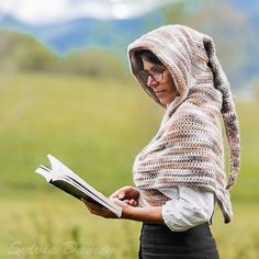 a woman in a knitted shawl is holding a book and looking at it