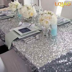 the table is set with silver sequins and white flowers