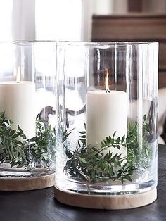 two glass vases with candles and greenery in them