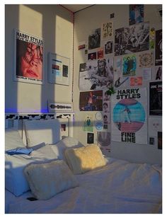 a bed with white sheets and pillows in a room filled with posters on the wall