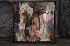 an art piece made out of wood and fabric with flowers on the bark in front of it