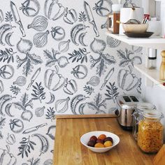 a bowl of fruit sitting on top of a wooden table next to a wall paper