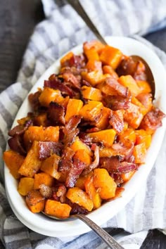 bacon and sweet potatoes in a white serving dish on a striped cloth with a wooden spoon