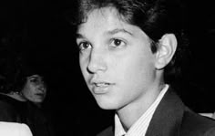 black and white photo of young man in suit with tie looking at camera while standing next to other people