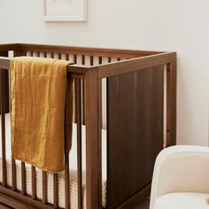 a baby crib with a yellow blanket hanging from it's side and a white chair in the foreground