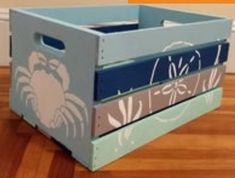 a wooden crate with an image of a crab painted on the front and sides, sitting on a hard wood floor