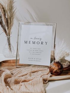 a memorial sign sitting on top of a table next to a vase with dry grass