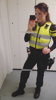 a woman in a yellow vest taking a selfie with her cell phone and holding a camera