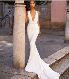 a beautiful woman in a white dress standing on some steps next to a pillar and tree