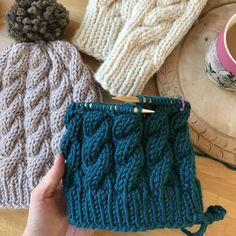 two knitted hats sitting on top of a wooden table next to a cup of coffee