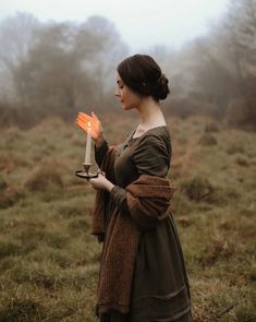 a woman is holding an orange candle in her hand while standing in a foggy field