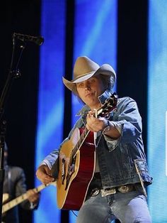 a man with a cowboy hat on playing guitar and singing into a microphone at a concert