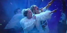 two women singing into microphones on stage with confetti falling from the sky