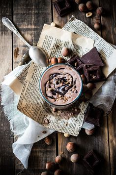 a bowl of chocolate and nuts on top of a newspaper with spoons next to it