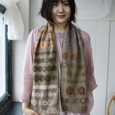 a woman standing next to a window wearing a scarf