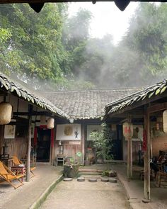 an outside view of a house in the middle of some trees with fog coming from the roof