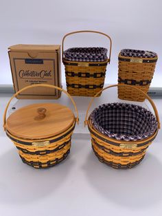 four woven baskets with wooden lids are sitting in front of a cardboard box and other items