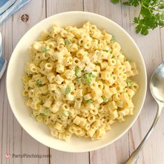 a white bowl filled with macaroni salad next to a spoon and parsley