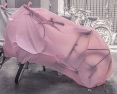 a bicycle covered with a pink sheet in front of a bike parked on the street