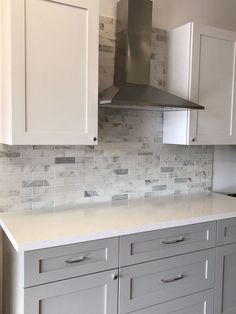 a kitchen with white cabinets and gray counter tops, stainless steel range hood over the stove