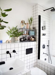 a white tiled bathroom with black accents and plants on the shelf above the bathtub