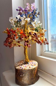 a tree with many colorful leaves on top of a wooden stump in front of a window