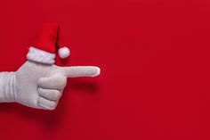 a hand in a santa hat pointing at something on a red background with the thumb down