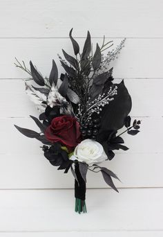 a bridal bouquet with black and white flowers, greenery and feathers on a white wooden background